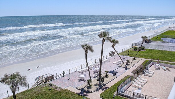 A beachside hotel with a patio area, palm trees, and ocean views.
