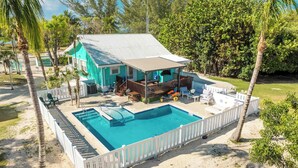 A turquoise house with a swimming pool, surrounded by a white fence and palm trees.