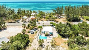 A beachfront property with a swimming pool, palm trees, and a view of the ocean.