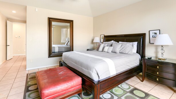 A bedroom with a bed, a wooden nightstand, a red bench, a ceiling fan, a mirror, and a lamp.
