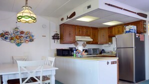 A kitchen with wooden cabinets, a stainless steel refrigerator, a microwave, and a coffee maker. - Just Steps to the Beach, this 3BDR Condo has Coastal Decor and Free WiFi and is Located on the North End of Town! (Ocean City)