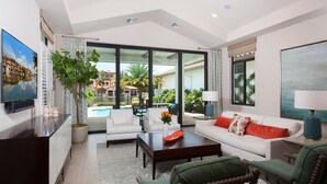 Ein großzügiges Wohnzimmer mit einem großen Fenster mit Blick auf einen Pool und eine Sitzgelegenheit im Freien.