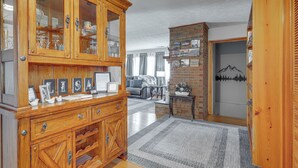 Un mueble de madera con puertas de cristal, una alfombra gris y una pared de ladrillo con una pintura de montaña.