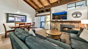 A spacious living room with a stone fireplace, a large TV mounted on the wall, and a cozy seating area with a sofa and chairs.
