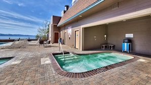 A rooftop pool area with lounge chairs, a hot tub, and a view of the mountains.
