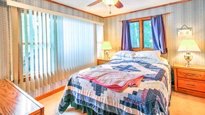 Ein Schlafzimmer mit einem Bett, zwei Nachttischen mit Lampen, einem Deckenventilator, einem Fenster mit Vorhängen und einem Holznachttisch.
