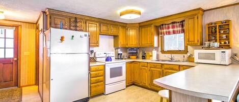 A kitchen with wooden cabinets, a refrigerator, stove, microwave, and a large island with stools.
