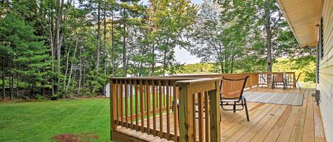 A wooden deck with a bench and chairs, surrounded by a grassy lawn and trees.