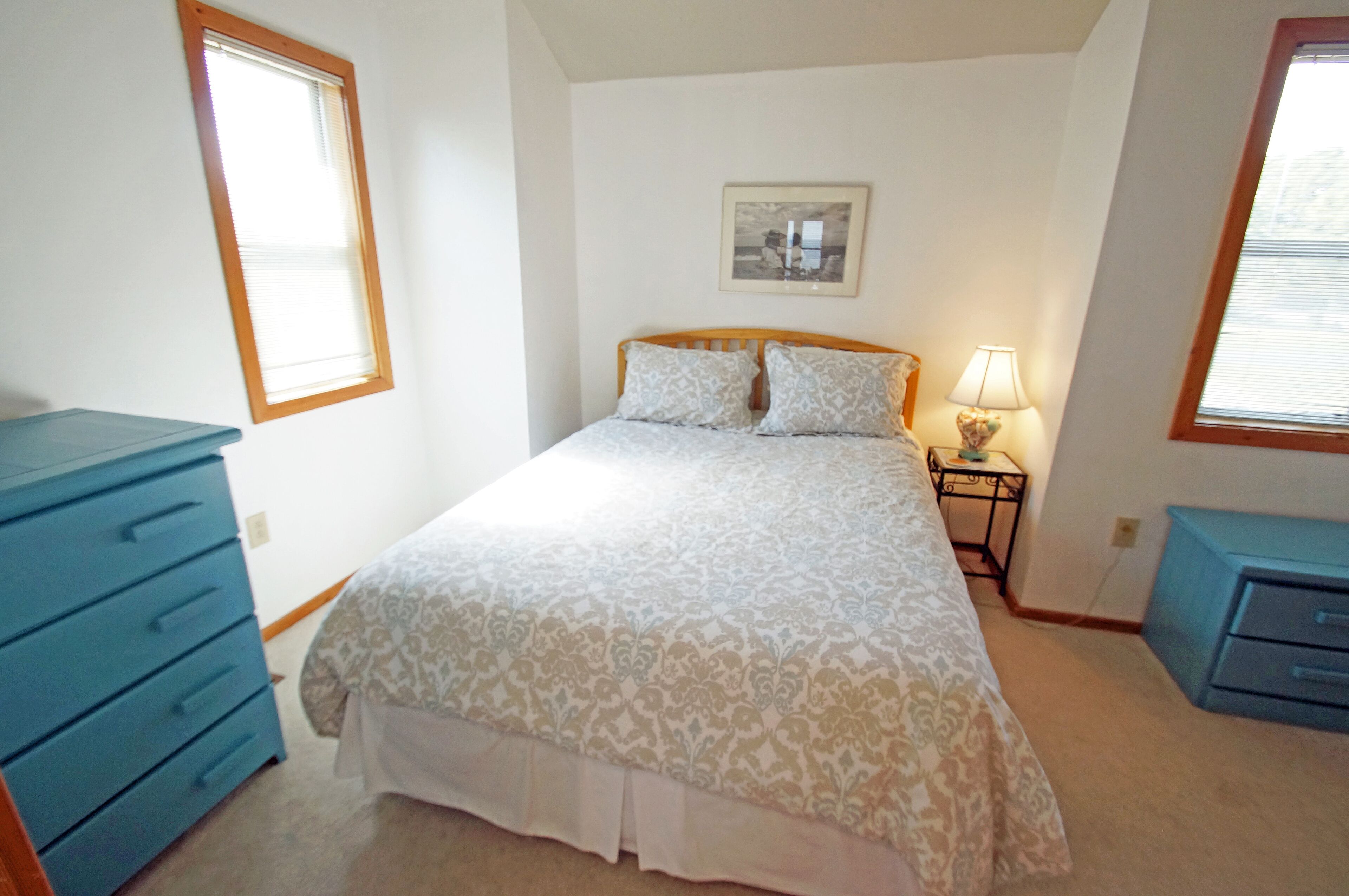 A bedroom with a bed, a nightstand with a lamp, a dresser, and a window.