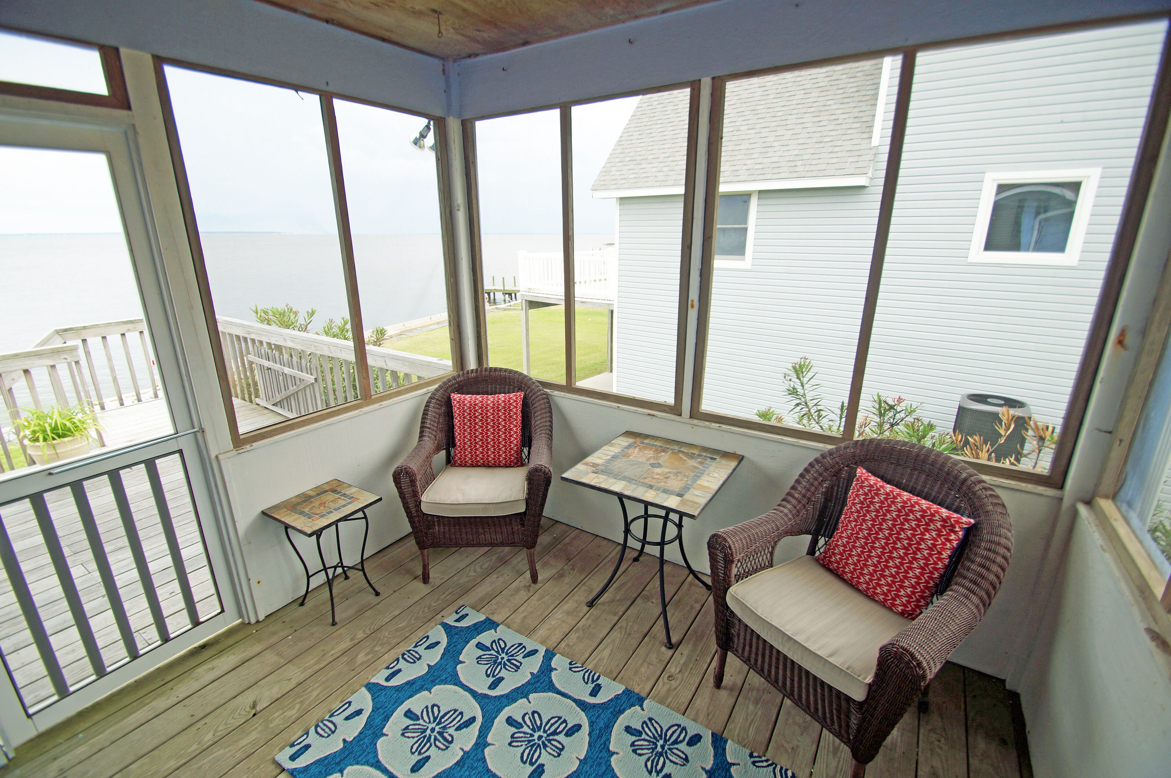 A covered porch with wicker chairs, a small table, and a view of the ocean.