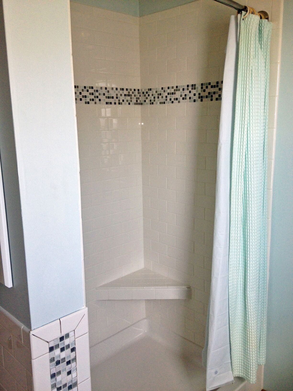 A shower area with white tiled walls, a tiled shower floor, and a shower curtain.