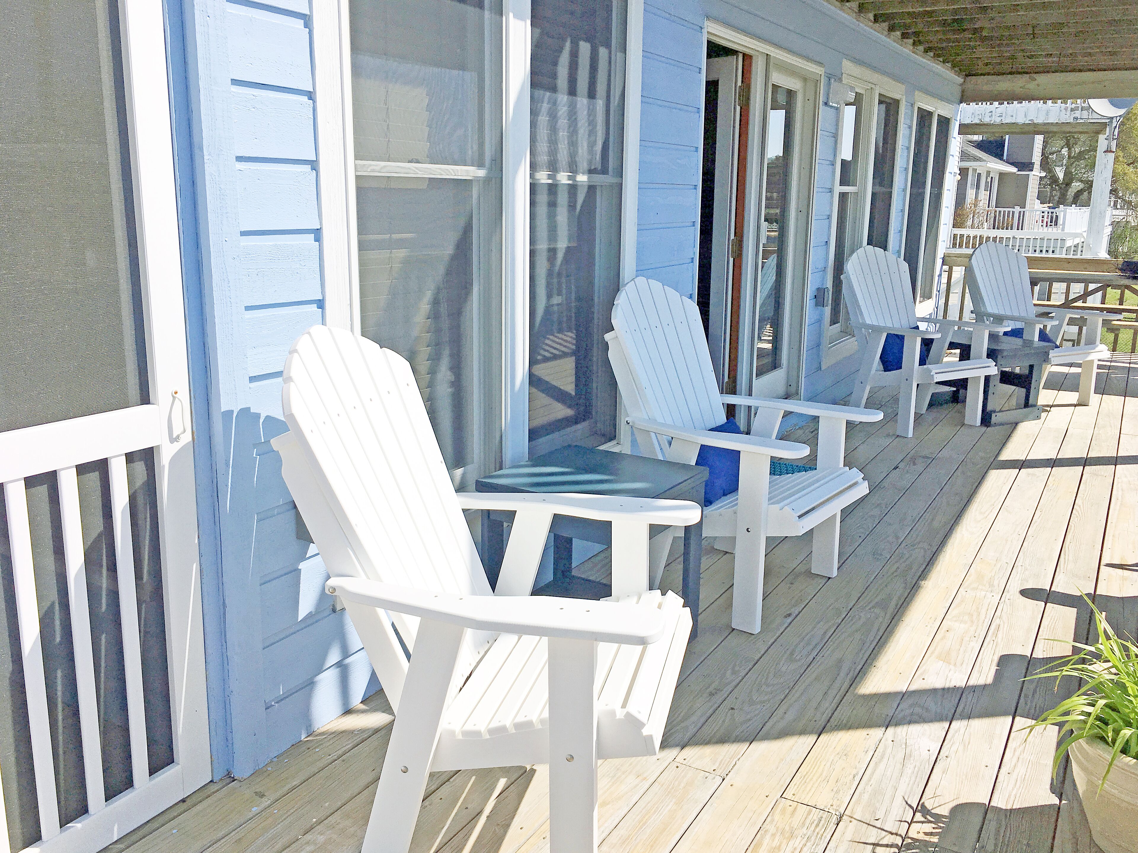 A covered outdoor seating area with white Adirondack chairs and a table, likely part of a resort or vacation rental property.