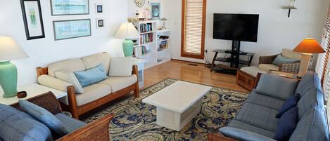 Un salon comprenant un canapé, des fauteuils, une table basse, une bibliothèque et un téléviseur.