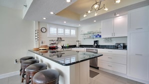 A modern kitchen with a central island, bar stools, and white cabinetry.