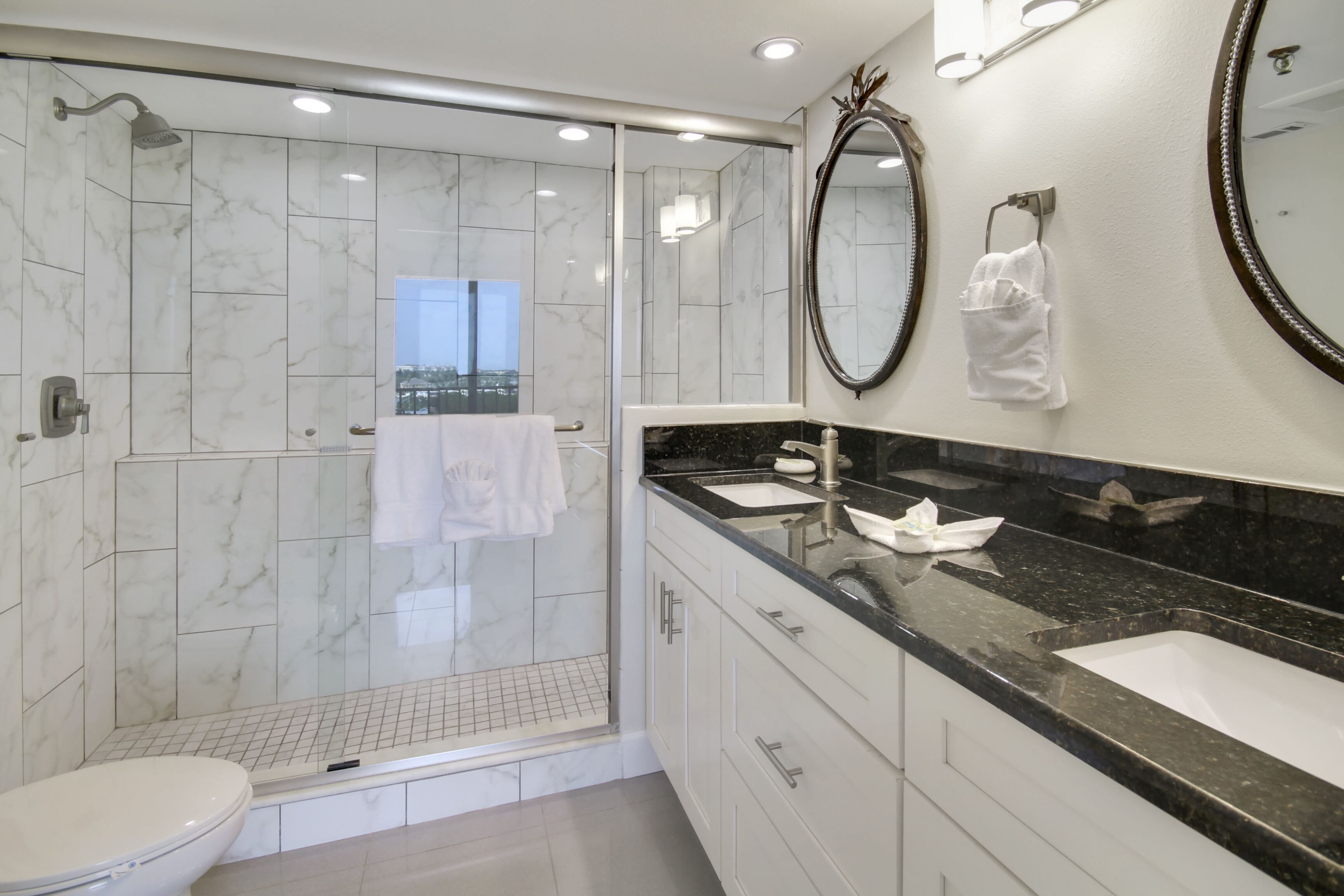 A modern bathroom with a glass-enclosed shower, a large mirror, and a vanity with a black countertop.