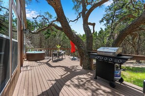 Una terraza de madera con un jacuzzi, una parrilla y una mesa con sillas.