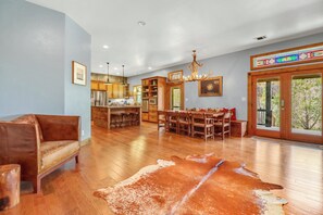 A spacious living area with a large wooden dining table, a leather sofa, and a cowhide rug.