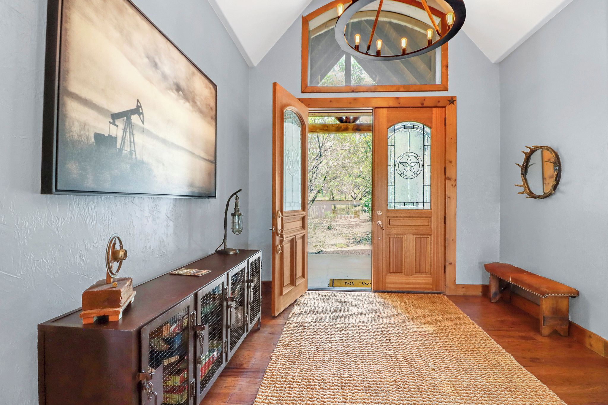 A spacious entryway with a wooden door, a large painting, a bench, and a rug.