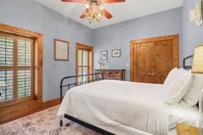 Ein Schlafzimmer mit Bett, Holzschrank, Deckenventilator und großen Fenstern.
