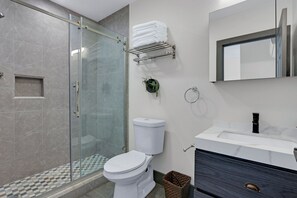 Un baño moderno con cabina de ducha de vidrio, inodoro blanco, lavabo con espejo y toallero con toallas dobladas.