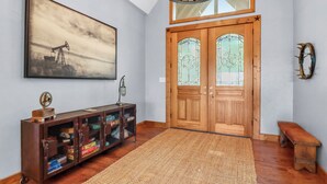 Um quarto com porta de madeira, tapete, um banco, armário com espaço para guardar objetos e um quadro na parede.