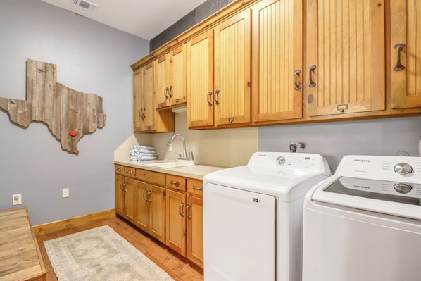 A laundry area with wooden cabinets, a sink, and two white washing machines.