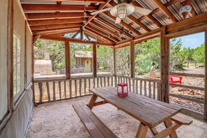 A covered patio area with a wooden table and benches, a red lantern, and a view of a garden with cacti and trees. - Southern Cross I Stargazing, hot tub, sleeps up to 8! (Wimberley)