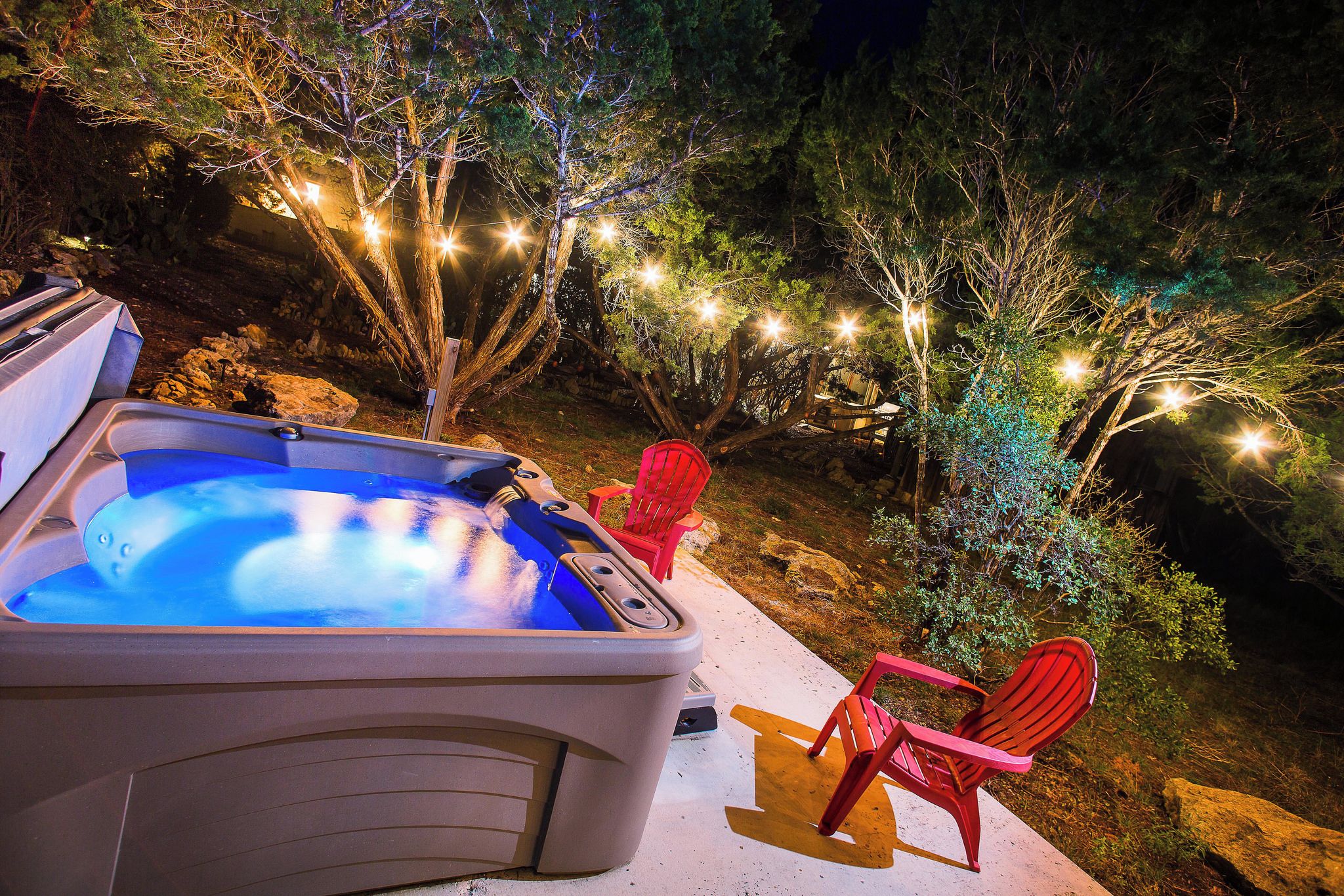 Un jacuzzi con dos sillas rojas, rodeado de árboles y luces colgantes.
