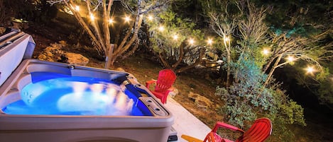 Un jacuzzi con dos sillas rojas, rodeado de árboles y luces colgantes.
