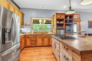 A kitchen with wooden cabinets, stainless steel appliances, a window with a view, and a hanging light fixture.