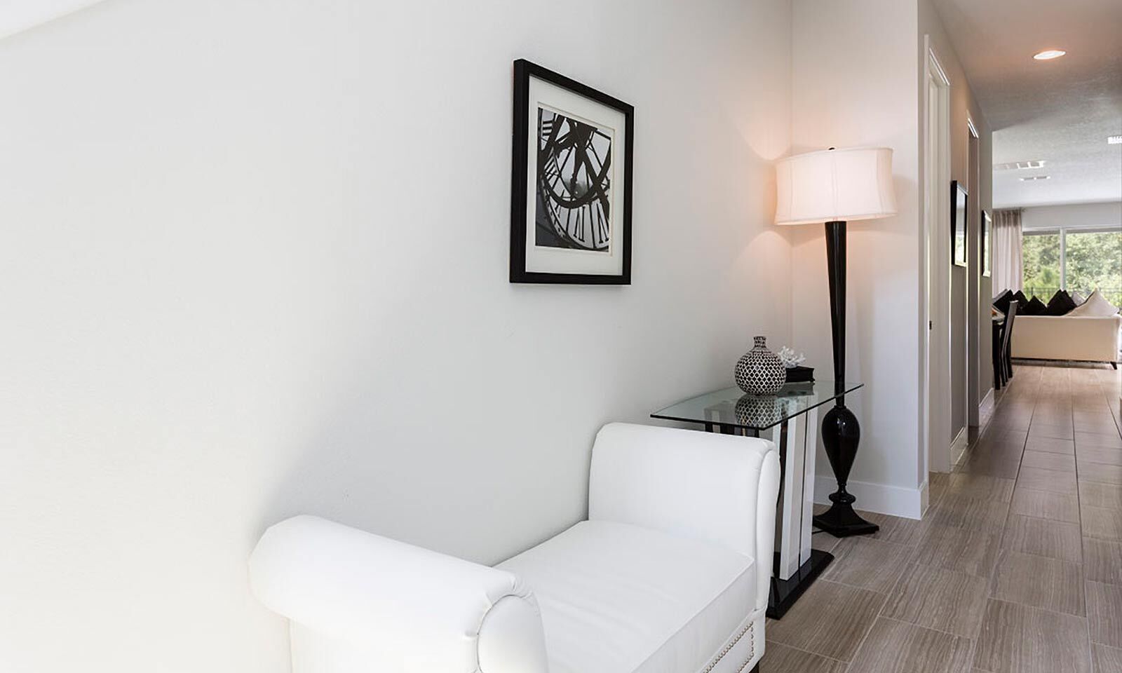 Ett modernt hotellrum med en vit soffa, ett glasbord med en vas, en golvlampa och ett inramat, abstrakt konstverk på väggen.