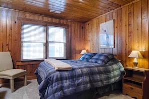 Un dormitorio con paneles de madera, una cama, dos lámparas de noche, una silla y un cuadro en la pared.