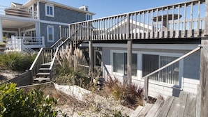 Una casa costera con una terraza de madera, una escalera que lleva a un balcón y vistas a la playa.
