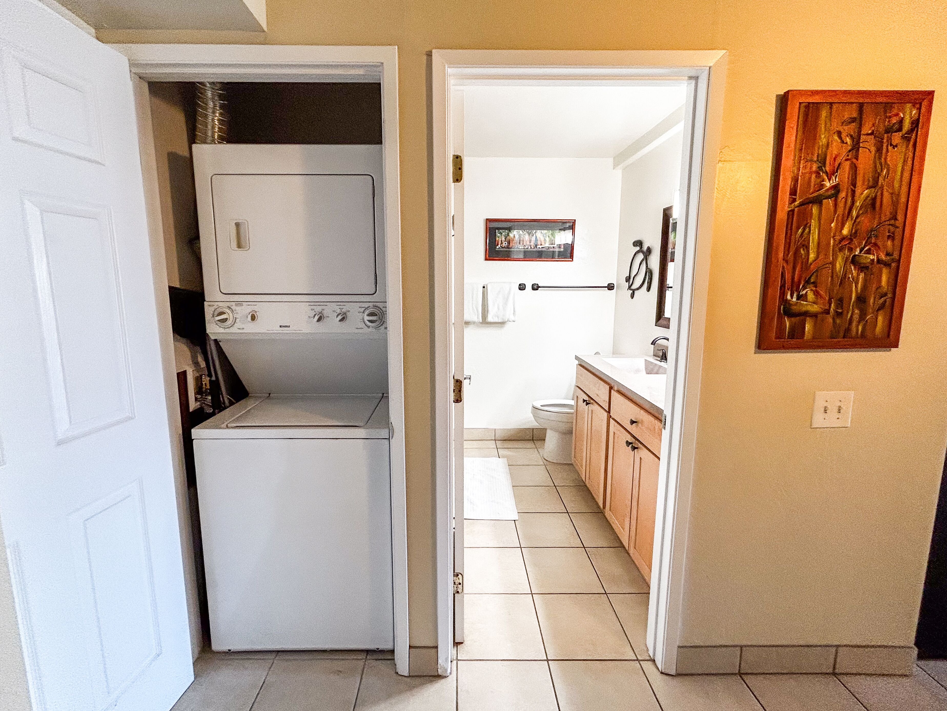 A laundry room with a washer and dryer, a bathroom with a toilet and sink, and a hallway leading to a bedroom.