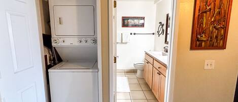 A laundry room with a washer and dryer, a bathroom with a toilet and sink, and a hallway leading to a bedroom.
