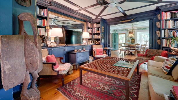 Ein geräumiges Wohnzimmer mit hoher Decke, Holzmöbeln und einem großen Bücherregal voller Bücher.