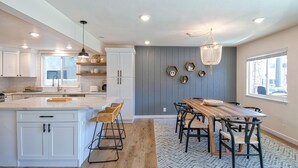 Una cocina moderna con armarios blancos, una isla grande y un comedor con mesa y sillas de madera.