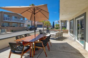 Une terrasse extérieure avec une table et des chaises en bois, un grand parasol et une vue sur la rue et les bâtiments voisins.