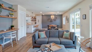 Una sala de estar moderna con un sofá gris, una mesa de centro de madera y un comedor con una mesa y sillas de madera.