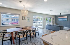 Un salon moderne doté d’une grande fenêtre, d’un coin repas avec une table et des chaises en bois, et d’un canapé gris.