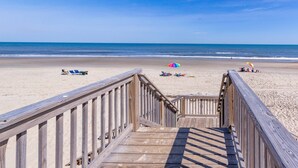 A wooden boardwalk leading to a sandy beach with umbrellas and lounge chairs.