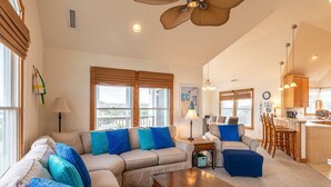A spacious living room with a sectional sofa, a coffee table, and a dining area with a kitchen in the background.