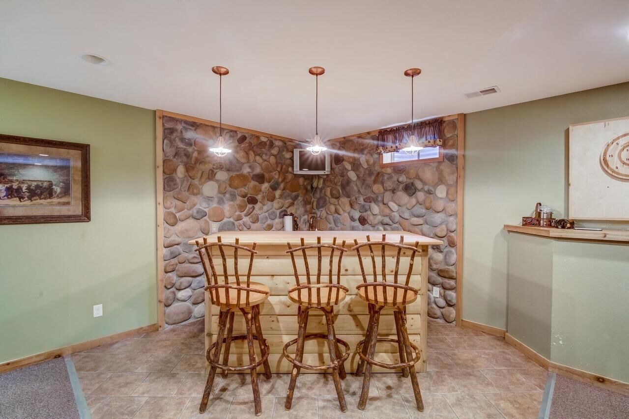 A bar area with a stone wall backdrop, three hanging lights, and a television.