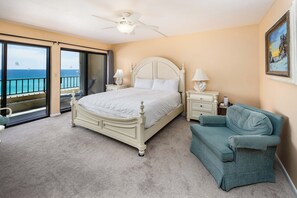 Een slaapkamer met een groot bed, een stoel, een nachtkastje en uitzicht op de oceaan door een schuifdeur.
