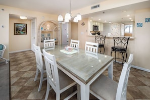 Uma sala de jantar com mesa de vidro, cadeiras brancas e um candelabro.