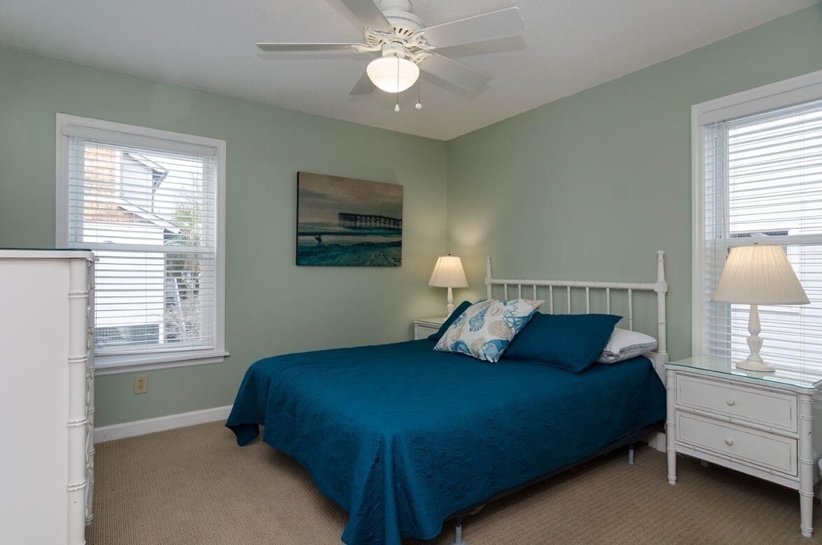 Une chambre à coucher avec un lit, une table de chevet, un ventilateur de plafond et un tableau accroché au mur.