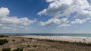 Ein Strand mit einer Holzlattenveranda, einem Pier in der Ferne und einem klaren Himmel.