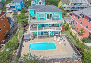 A two-story building with a swimming pool, multiple balconies, and a fenced deck area. - Milo's Waves - Corolla, Ocean Sands, 50 Yards to Beach, Pool, Hot Tub, Pets OK (Corolla)