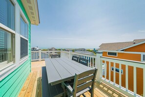 A wooden deck with a table and chairs, overlooking a beach with houses in the background. - Milo's Waves - Corolla, Ocean Sands, 50 Yards to Beach, Pool, Hot Tub, Pets OK (Corolla)