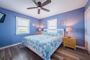 A bedroom with a bed, two windows, a ceiling fan, a nightstand, and a door. - Milo's Waves - Corolla, Ocean Sands, 50 Yards to Beach, Pool, Hot Tub, Pets OK (Corolla)